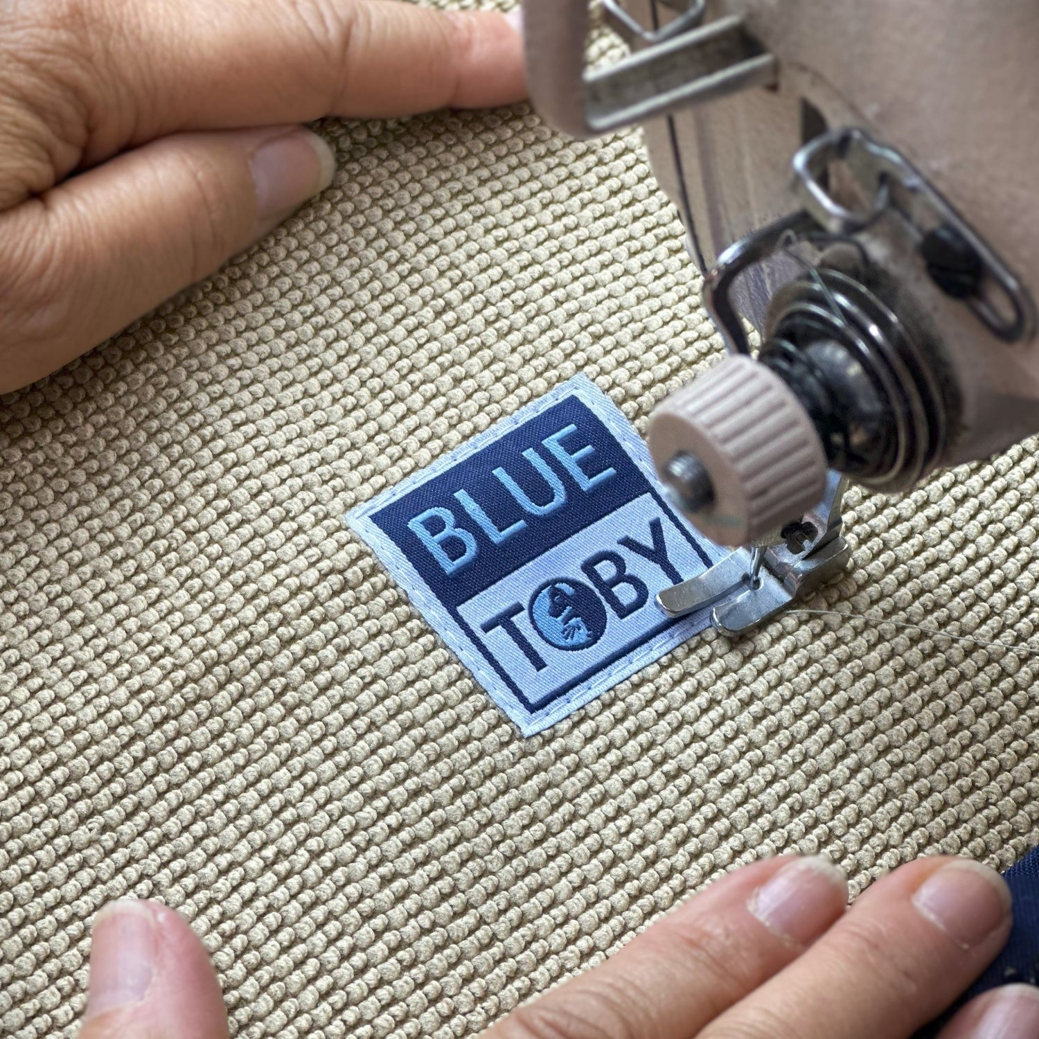 Close up view of sewing Blue Toby tag on bed