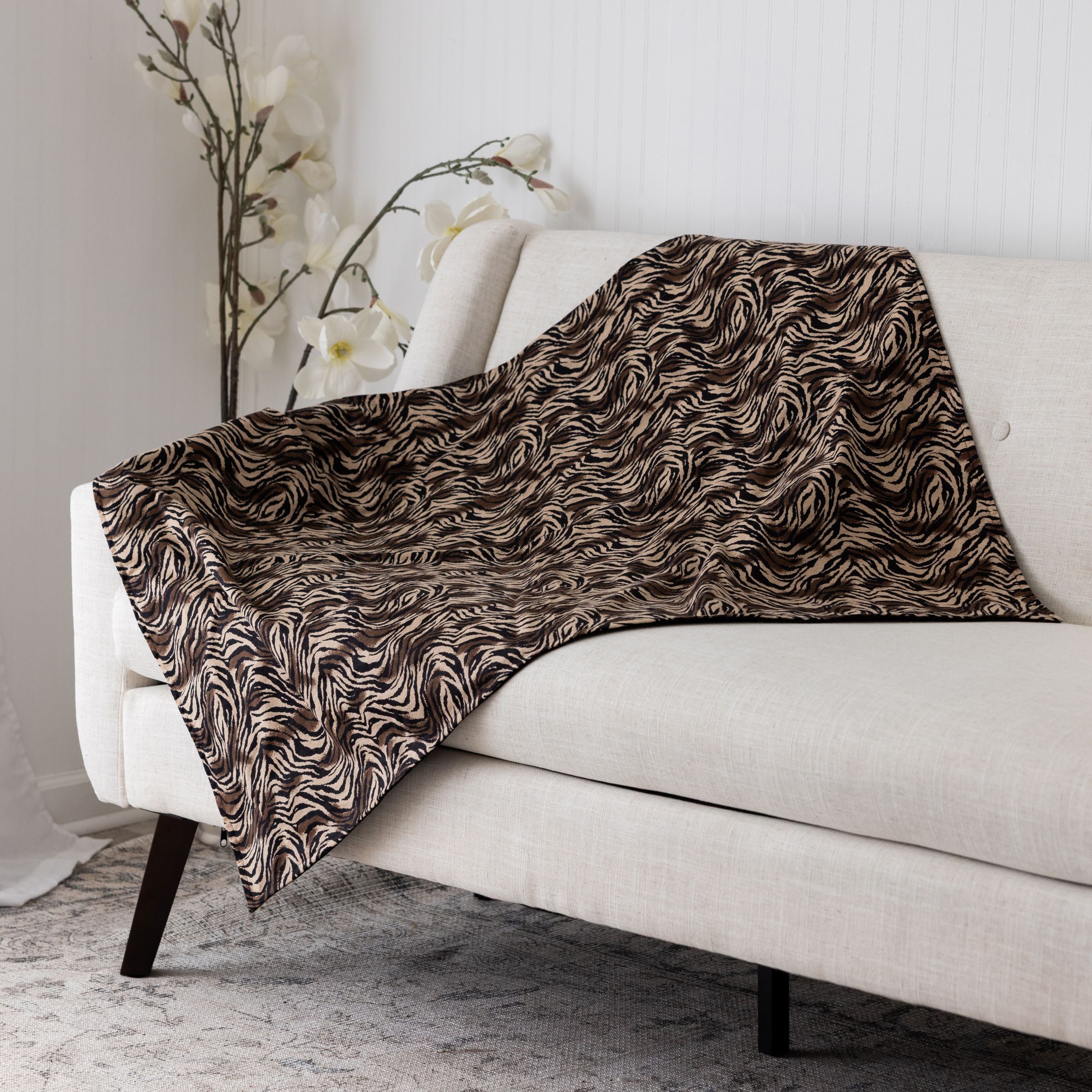 Blue Toby cotton flannel zebra  patterned throw blanket draped over a white sofa with a neutral background.