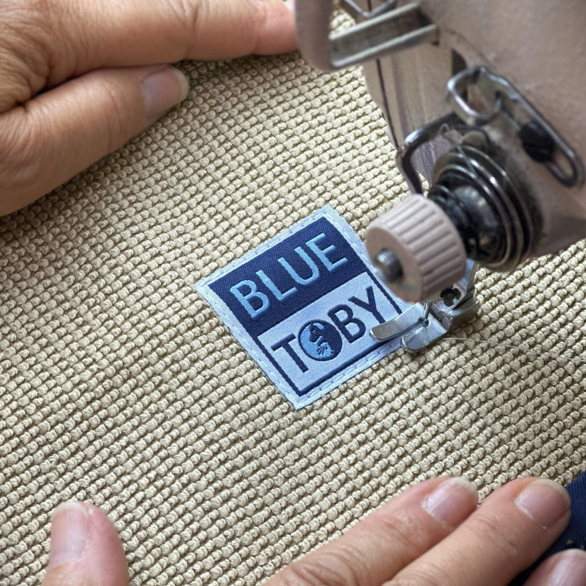 Sewing machine needle close-up with a 'Blue Toby' label on beige eco-friendly fabric.
